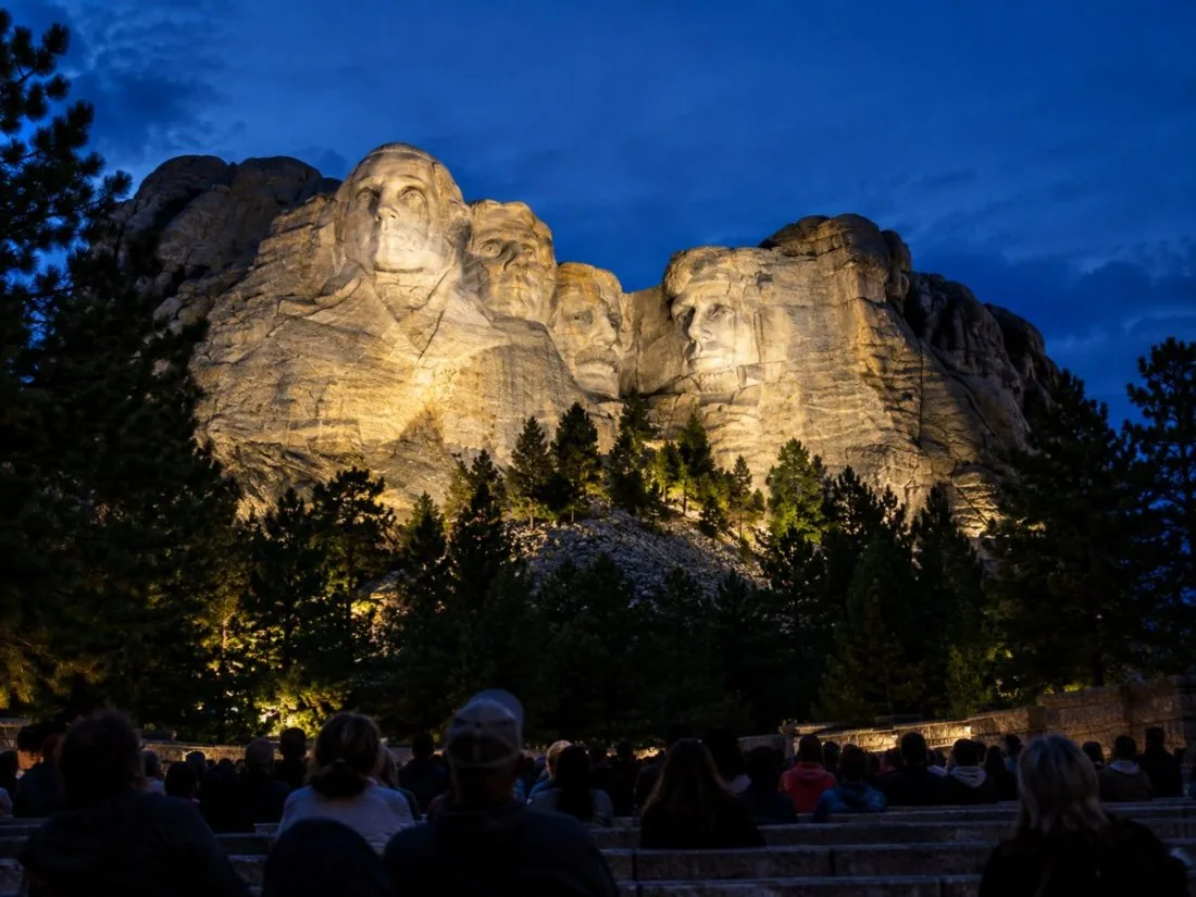 Mount Rushmore éclairé par des projecteurs au crépuscule au-dessus d'un amphithéâtre en plein air